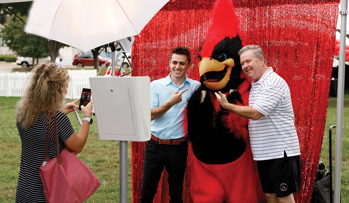 student and parent pose for a photo with Red the cardinal, CUA's mascot