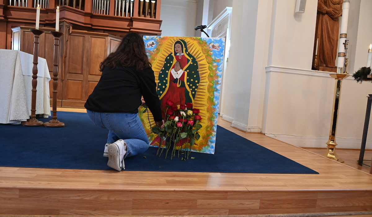 student putting flowers by a painting of Our Lady of Guadalupe