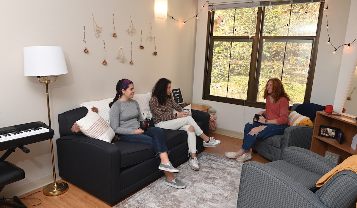 Three girls talk in the living room of their Opus Hall apartment