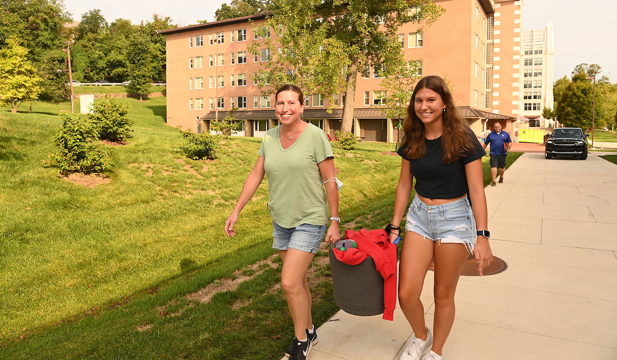 a student and her mother carry a basket together as they move into a freshman dorm