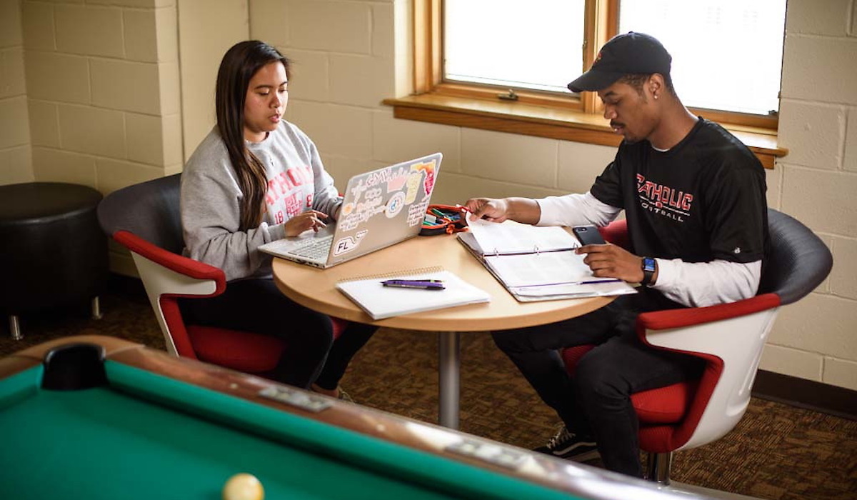 A male and female student do homework at a table in the McDonald House lounge