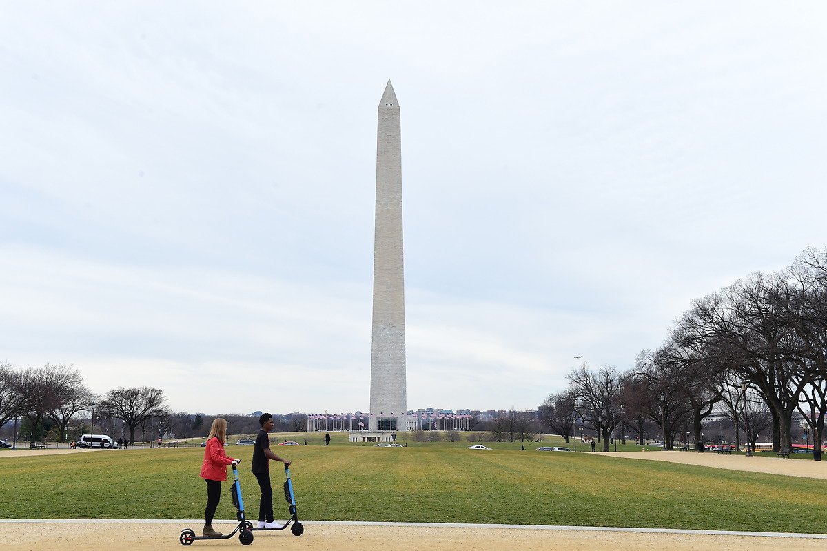 Students ride scooters in front of Washington Monument.
