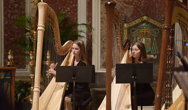 A professor conducts a quarter of students playing the harp.