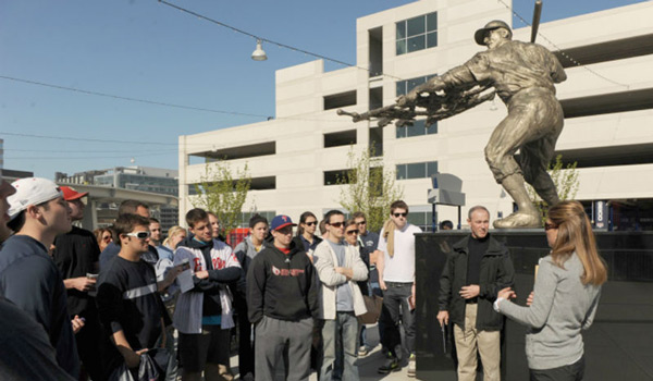 A Catholic University class standing next to a baseball statue on a class outing.