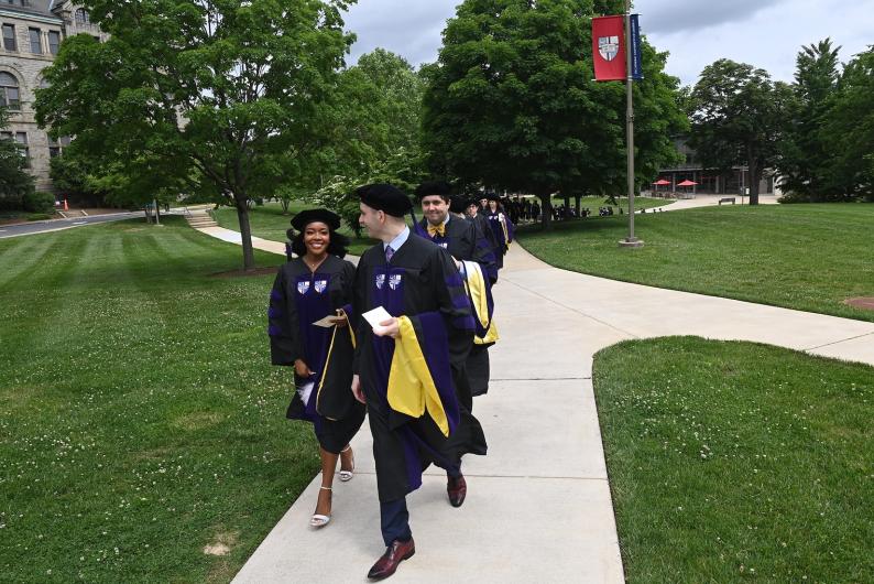 law school graduates walking across campus in their graduation caps and robes
