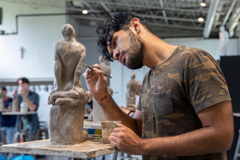 student sculpting a sculpture of a woman out of clay
