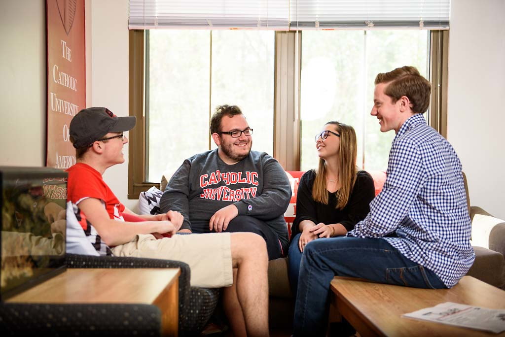 Four students talking and smiling in a dorm living room.