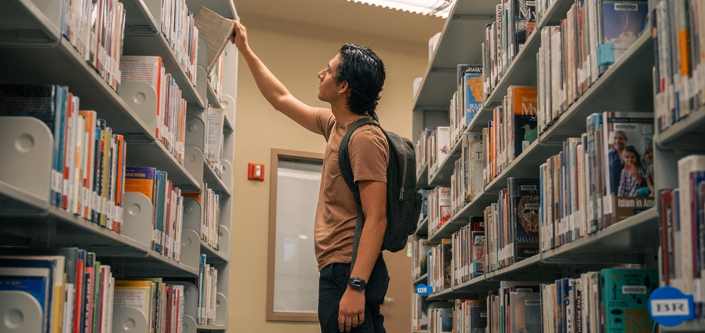 student pulling book off of library shelf
