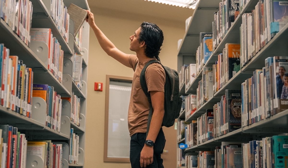 student pulling book off of library shelf