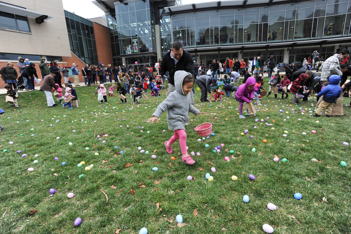 Toddler picking up easter eggs on the Pryz lawn while father smiles in enjoyment